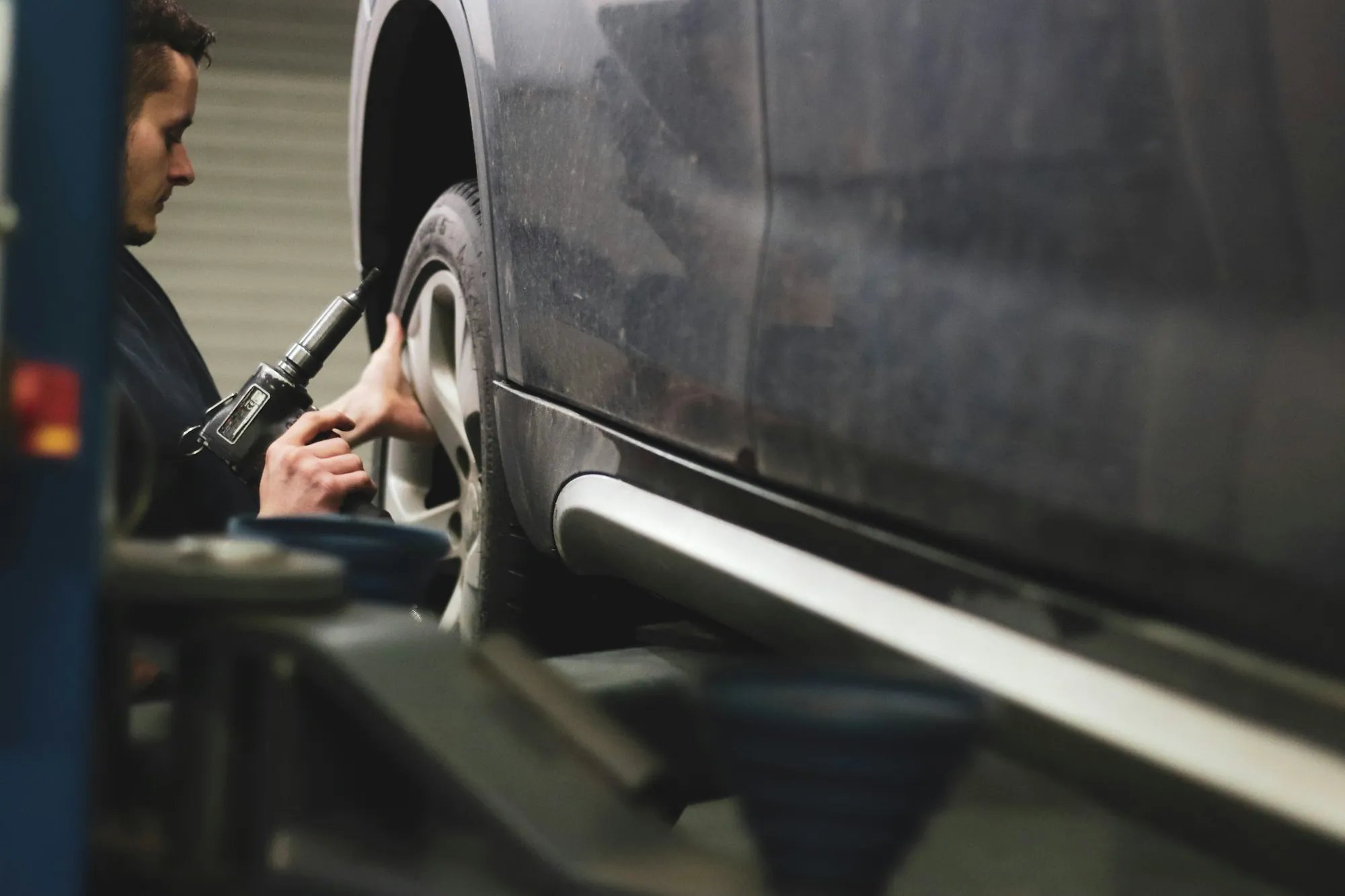 Technician inspecting the side of a dark car in a shop